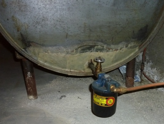 This fuel oil storage tank in a home's basement has been patched, as evidenced by the non-matching color of the tank near the valve.